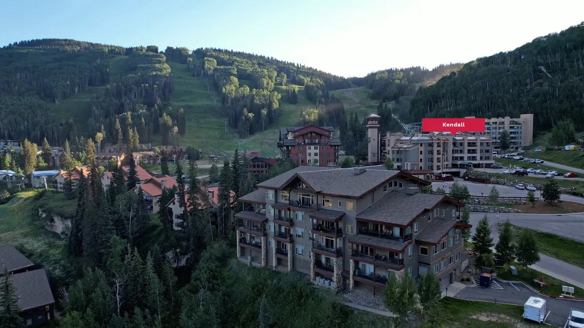 A tranquil exterior scene highlights luxury buildings surrounded by wooded areas and expansive mountain views. The soft morning light and untouched nature evoke opportunities for hiking, wildlife watching, and exploring beyond the winter season.