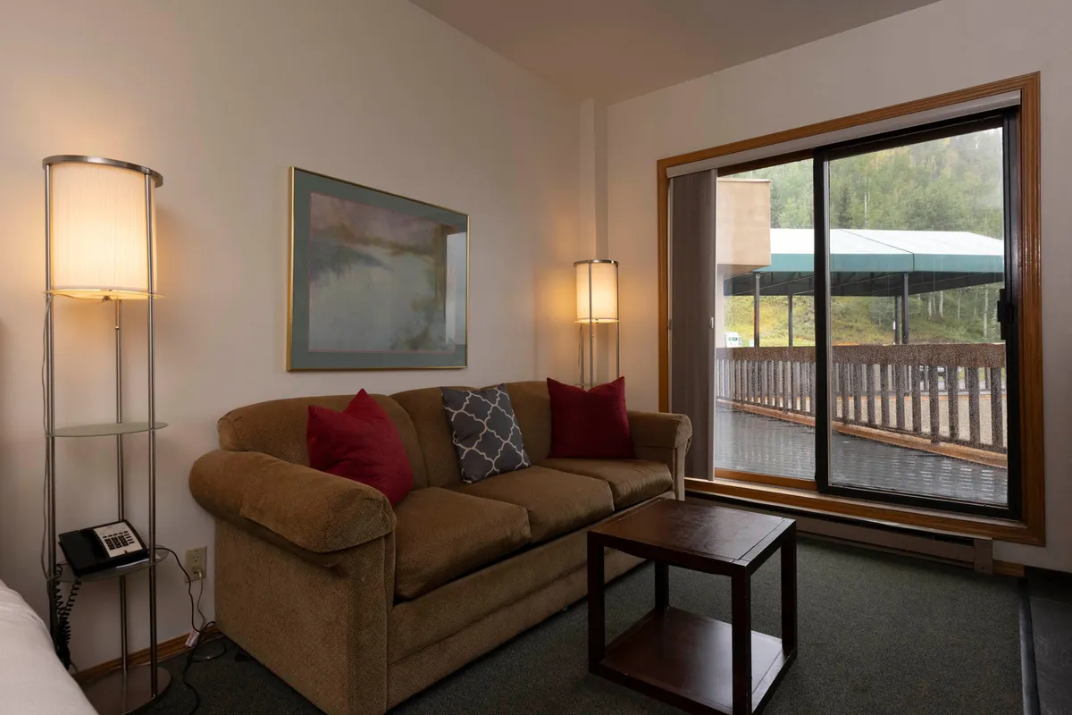 A bright and inviting living area with a plush sofa, coffee table, and large windows flooding the room with light. Floor lamps and tasteful decor create a welcoming space, perfect for conversation, laughter, or peaceful solitude. The scene exudes comfort and connection.