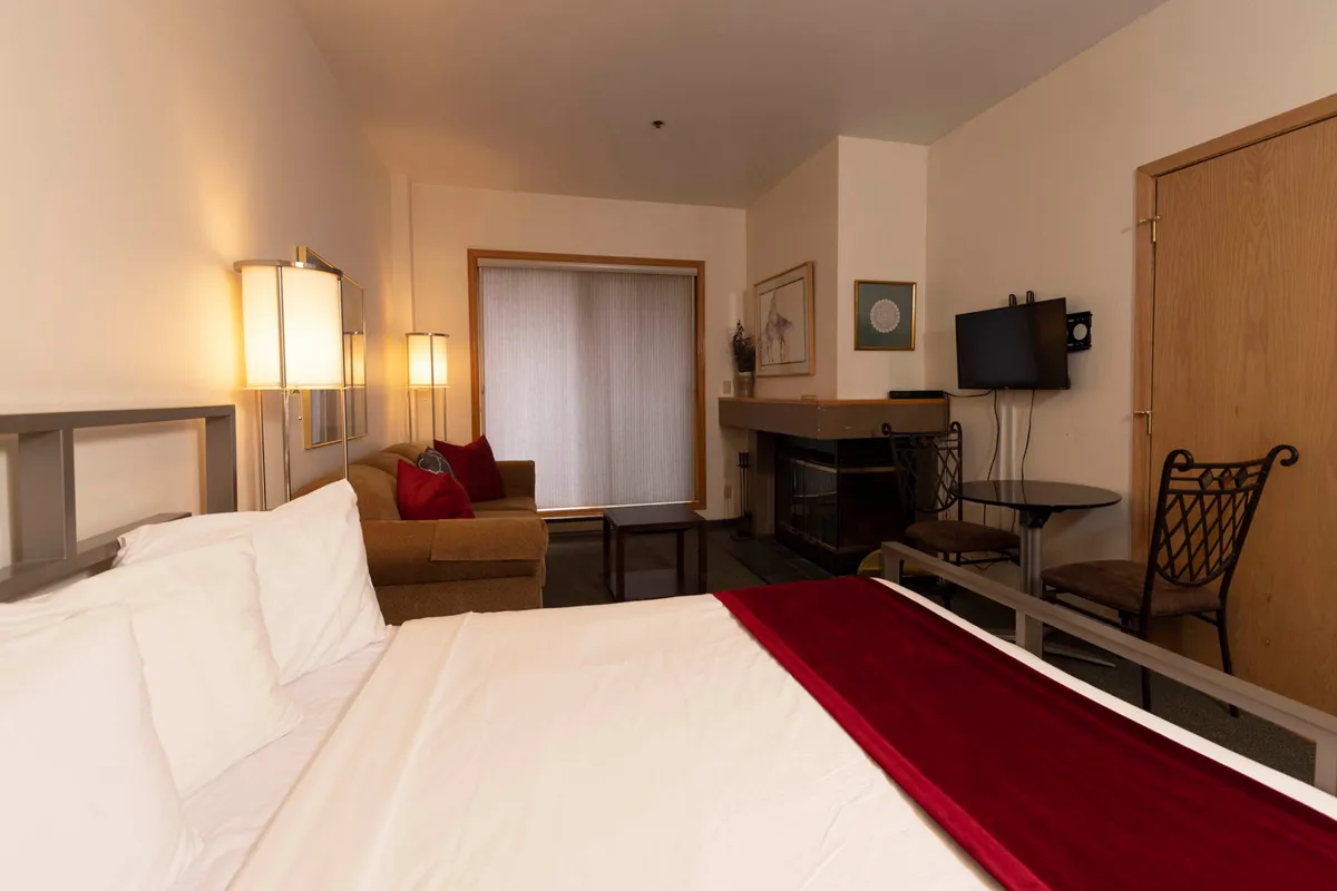 This image shows a welcoming bedroom featuring a comfortable bed, a cozy fireplace, a seating area, and a TV. The soft lighting, plush linens, and warm touches create an inviting and tranquil atmosphere. The fireplace adds a romantic lodge-style ambiance, making the space ideal for relaxation after a day in the mountains.
